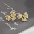 Elegante goldene Schleifen-Ohrstecker mit gebürsteter Textur und Herz auf grauem Papier - Gold (ED897506)