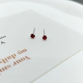 Close-up of elegant small red zircon stud earrings with silver four-prong setting - Garnet Red