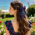 Sweet navy blue hair clip with cherry print bow shown on model in a sunny garden setting - Navy Blue Background Red Cherry Print / Dark Blue