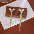 Elegant gold bow earrings with crystal tassel drops shown on a wooden display board - Gold Bow Crystal Tassel