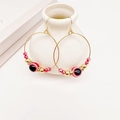 Goldene Evil Eye Creolen mit roten Perlen und Strass auf einem Keramikständer - Rot