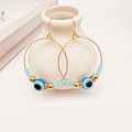 Golden hoop earrings with evil eye beads and crystal spacers on a white vase - Lake Blue
