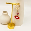 Detail of golden Evil Eye keychain with two red enamel charms on a display stand - Red Style 7