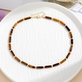 Detail van tijgeroog kralenketting met gouden kralen en karabijnsluiting op wit dienblad - Tijgeroog bruingeel Stijl B