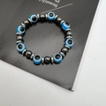 Elastisches Armband mit blauen Augen-Perlen und dunkelgrauen Hämatitsteinen auf dunklem Grund - Seeblau