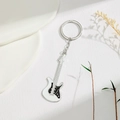Detailed macro of white electric guitar keychain with black pickguard on white texture - White