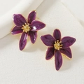 Detalle macro de pendientes de flores de esmalte morado con centro dorado sobre piedra - Púrpura