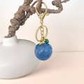 Sparkly blue apple keychain with golden hardware hanging on a decorative branch - Blue Apple