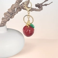 Sparkly red apple keychain with gold clasp hanging on a branch over pink background - Red Apple