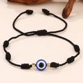 Detail macro-opname van geweven Evil Eye armband met blauwe kraal en goudkleurige kralen - Zwart Touw Enkel Oog