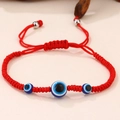 Dettaglio di un bracciale intrecciato rosso con ciondoli occhio blu e perline di metallo argento - Tre Occhi Corda Rossa