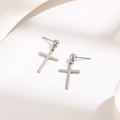 Minimalist silver cross drop earrings with polished spherical studs on white fabric - Silver