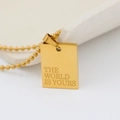 Detailed macro view of the gold rectangular pendant with The World Is Yours engraving - THE WORLD IS YOURS (New)
