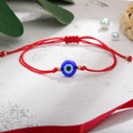 Detailweergave van een rood gevlochten Evil Eye armband met blauwe kraal op marmer - Dubbele Koord Boze Oog / Dubbele Rode Koord Gouden Kralen (B2658)