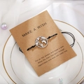 Detail eines gewebten Weltkarten-Armbands mit schwarzer Kordel auf einer Wunschkarte - Silberne Karte (B2505)