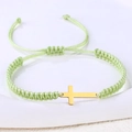 Nahaufnahme des handgewebten minzgrünen Armbands mit einem polierten Goldkreuz-Anhänger - Edelstahl Gold Kreuz (B3421)