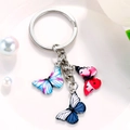 Detail of silver keychain with three colorful butterfly charms on white porcelain dish - Pink Light Blue Dark Blue Textured Butterfly Style (M744)