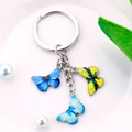 Close-up of a silver keychain featuring three colorful enamel butterfly pendants - Royal Blue Light Blue Bright Yellow Textured Butterfly Style (M750)