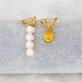 Close-up of asymmetrical gold earrings featuring freshwater pearls and yellow pear-cut zircon - Yellow