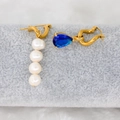 Detailed close-up of asymmetric gold earrings with white pearls and a blue teardrop zircon - Sapphire Blue