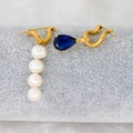 Detail view of gold earrings with drop zircon and pearls on a grey velvet roll - Dark Blue