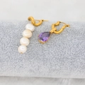 Detailed shot of gold twisted hoop earrings with white pearls and purple drop zircon - Deep purple