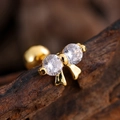 Macro shot of gold-plated bow earring with zircons and ball back on wooden texture - Double Zirconia Bow Style (3134) / Gold