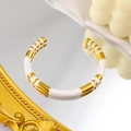 Macro view of C-shaped bamboo gold bangle with white enamel inlay on reflective surface - White