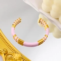 Detail of a C-shaped 18K gold-plated bangle with pink enamel stripes on a reflective surface - Pink