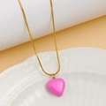 Detailed close-up of a pink heart pendant on a gold snake chain over a white ceramic plate - Pink