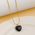 Macro shot of a black heart pendant necklace with golden snake chain on white porcelain - Black