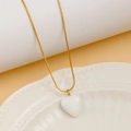Detailed macro of a gold snake chain necklace with a white enamel heart pendant on a plate - White