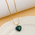 Close-up of green heart pendant on gold snake chain resting on white ceramic tray - Dark Green
