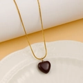 Detail of dark heart pendant on gold snake chain resting on white embossed ceramic plate - Coffee