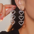 Dettaglio di orecchini a triplo cuore in argento con cristalli lucidi sulla modella - Stile Pendente a Triplo Cuore con Strass (BXE018S)