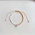 Detail van verstelbare kralenarmband met witte vierkante kralen en gouden letter E bedel - Letter E (BLS220006E)
