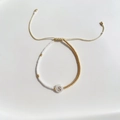 Detail van een kralenarmband met witte en gouden kralen en een S-letterbedel - Letter S (BLS220006S)