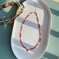 Detail van rode kralenketting met hartvormige hanger op een wit keramisch bord bij daglicht - Rode Kralen Rode Hart Hanger (SJX220012B)