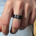 Detalle de un anillo de acero inoxidable negro mate con la letra R plateada en la mano - Talla 6 / Estilo Letra R (M566-R) / Negro