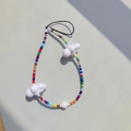 Macro detail of colorful beaded phone strap with white cloud charms on grey background - Colorful