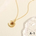 Detalle del collar dorado con luna, estrella y circón rojo sobre fondo con textura - Oro con piedra principal marrón rojizo (NE2146-A-1)