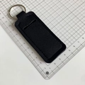 Detail view of black neoprene lipstick holder keychain with metal ring on measuring grid - Black