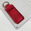 Detail of red neoprene lipstick holder keychain with metal ring on cutting mat - Red
