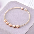 Macro detail of a 14K gold plated wire wrapped bracelet with seven natural pink pearls - Gold Pink Orange Pearl Open Bangle / Gold