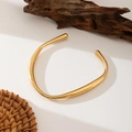 Collar rígido dorado de acero inoxidable pulido sobre un fondo natural minimalista - Brazalete abierto irregular en forma de C (E269) / Dorado