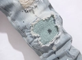 Detail of distressed light blue denim jeans with green pleated patch and paint splatters - Standard Style (Original AM) / Blue