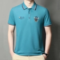 Detailed view of lake blue polo shirt with embroidered badge and striped collar accents - Denim Blue