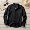 Detail of black linen shirt showing stand collar, chest pocket and white buttons on wood surface - S / Black