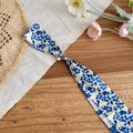 Close-up view of a blue floral silk scarf necklace with an adjustable pearl buckle - Blue and Yellow Print