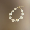 Primer plano de una pulsera de cuentas de concha irregular con una cadena dorada - Capa Simple / Blanco